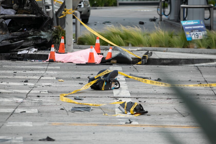 A body covered with a sheet lies in the street next to debris and the burnt-out wreckage of a vehicle