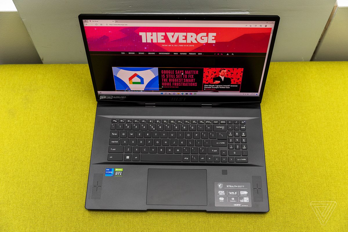 The MSI GS77 Stealth keyboard seen from above on a yellow fabric bench.  The screen displays The Verge home page.