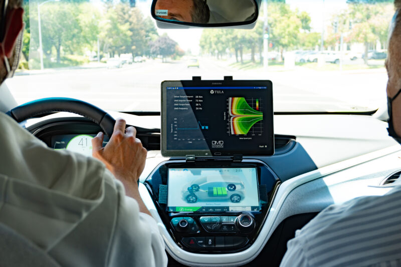 An iPad is mounted on the dashboard of a Chevrolet Bolt.  Two men occupy the front seats, each wearing a face mask.